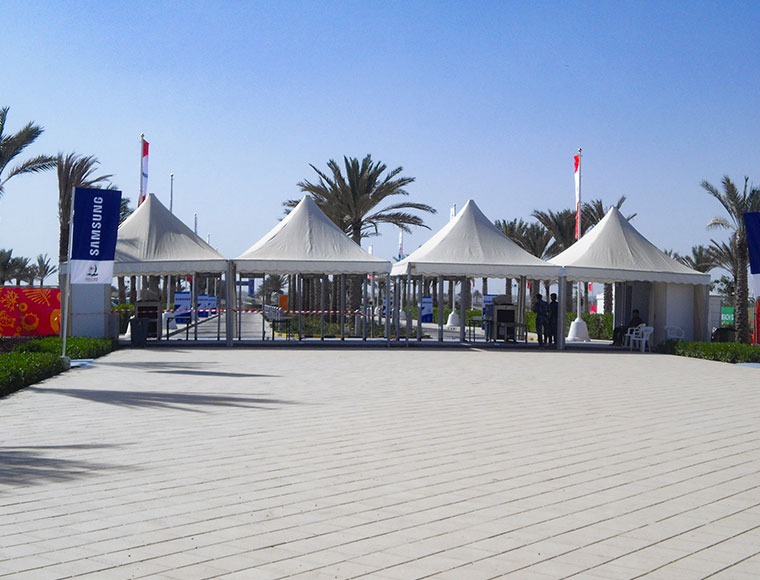 Row of white pagoda tents on a sandy beach with calm sea in the background